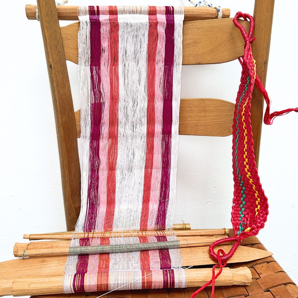Wooden chair with a loom in white and magenta and colorful yarn on a white background