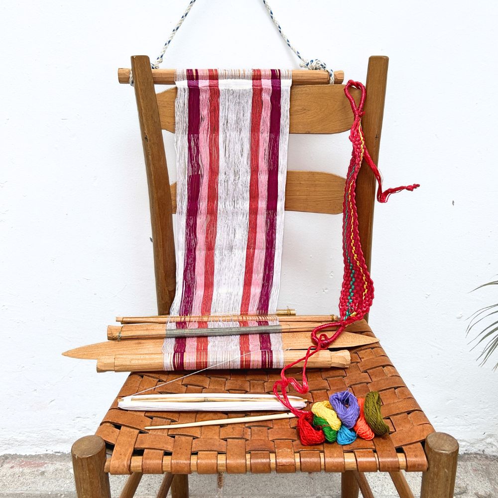Wooden chair with a loom in white and magenta and colorful yarn on a white background