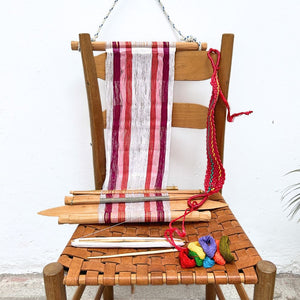 Wooden chair with a loom in white and magenta and colorful yarn on a white background