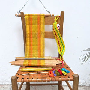 Wooden chair with a loom in yellow and colorful yarn on a white background