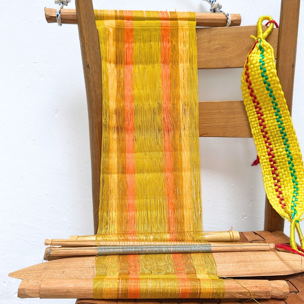 Wooden chair with a loom in yellow and colorful yarn on a white background