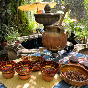 Ceramic pots and bowls on a table with a fountain and greenery in the background