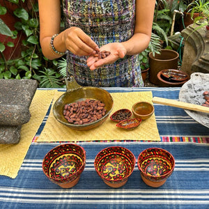 Freshly roasted cacao beans ready to be peeled, displayed alongside traditional jícaras and the spices that will be ground together with the cacao.