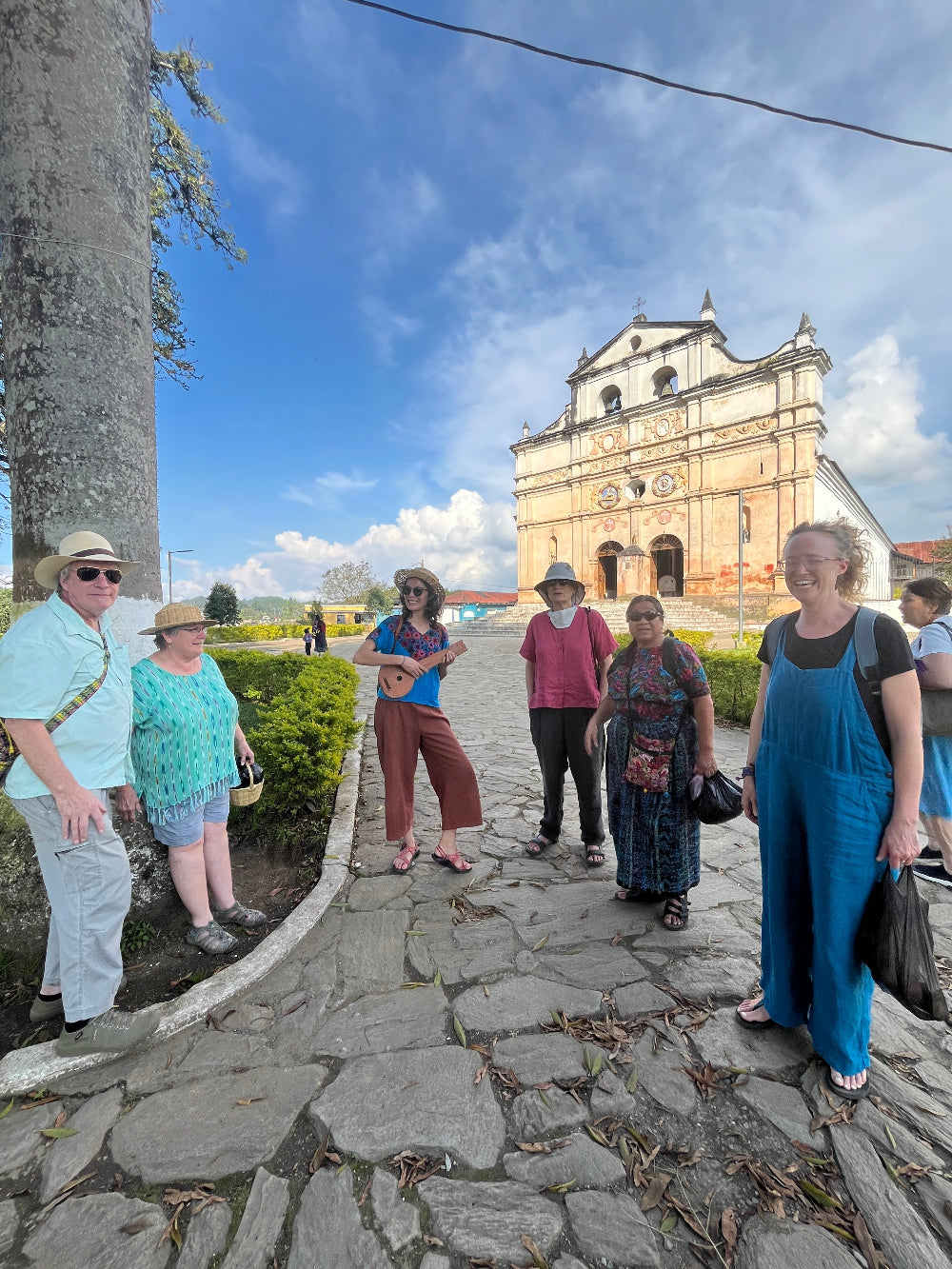 Group smiling in front of a historic church, next to a large ceiba tree.