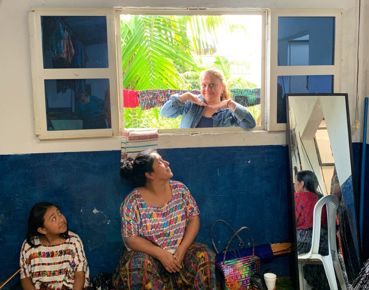 A smiling woman looks through from a window, with weavers smiling back