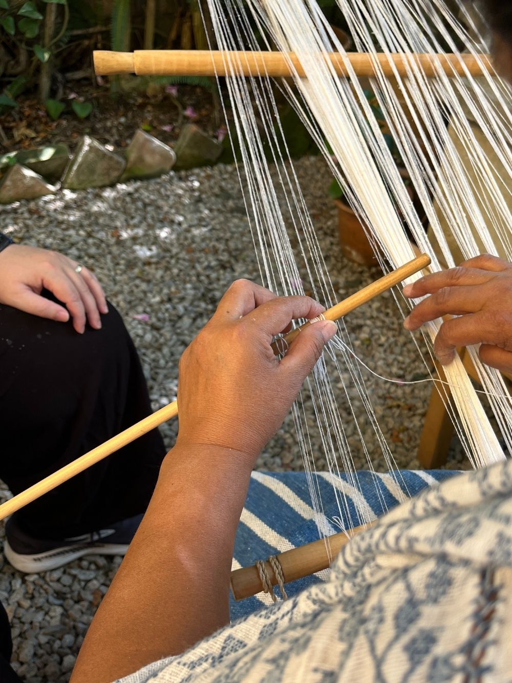 Person weaving with a loom outdoors