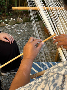 Person weaving with a loom outdoors