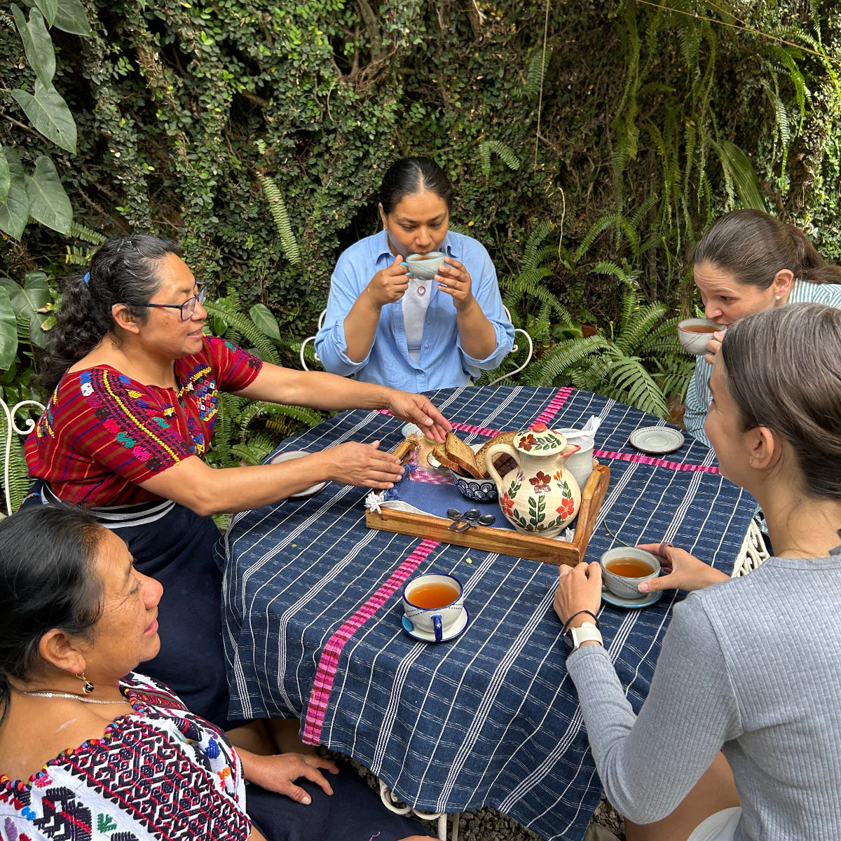 Group of people gathered around a table drinking tea, outdoors.