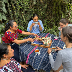 Group of people gathered around a table drinking tea, outdoors.