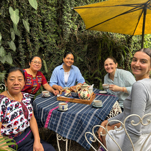 A group of five posing outdoors with a yellow umbrella and greenery.