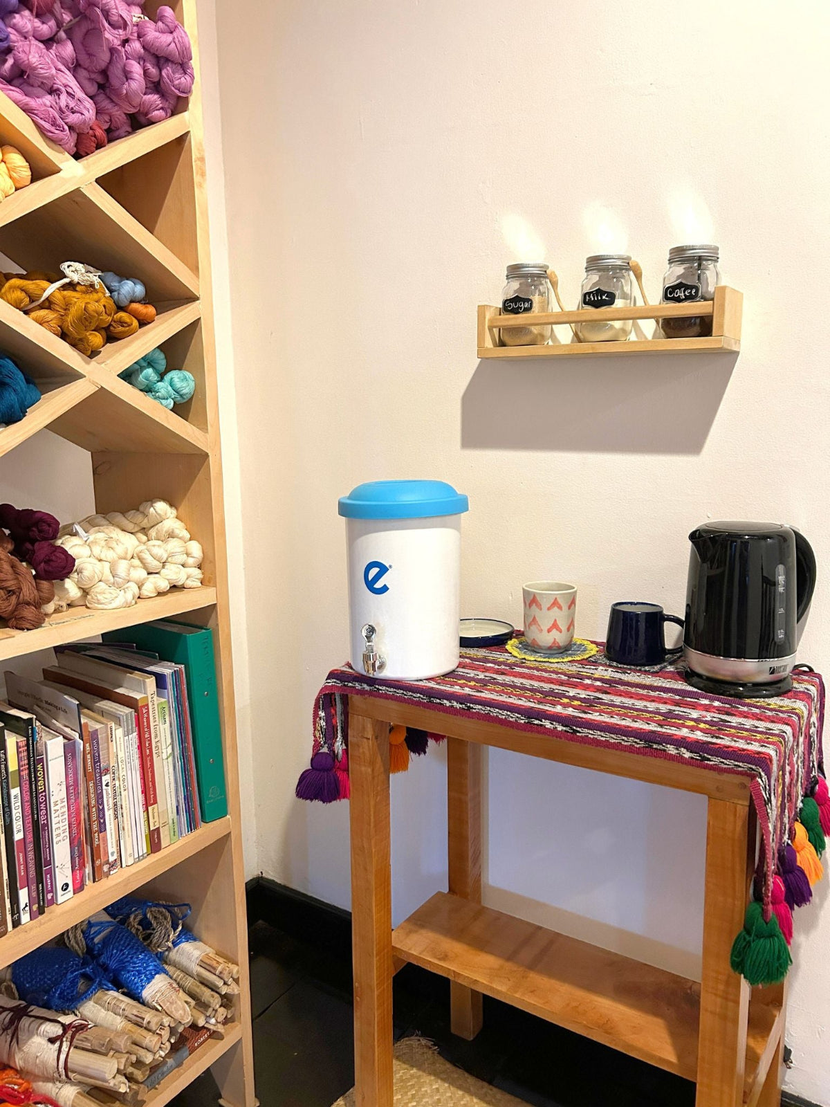 Small table with kitchen items next to a bookshelf filled with books and threads.