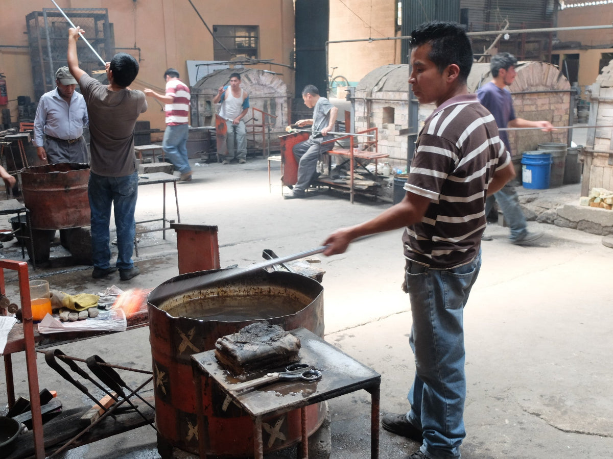 Workers in a glass workshop with large metal containers and tools
