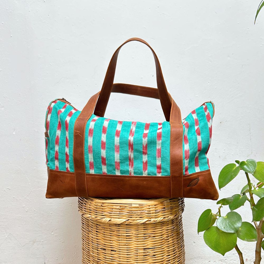 Duffel bag in green and red striped pattern textile with leather on a white background