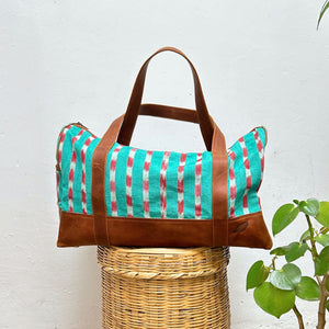 Duffel bag in green and red striped pattern textile with leather on a white background