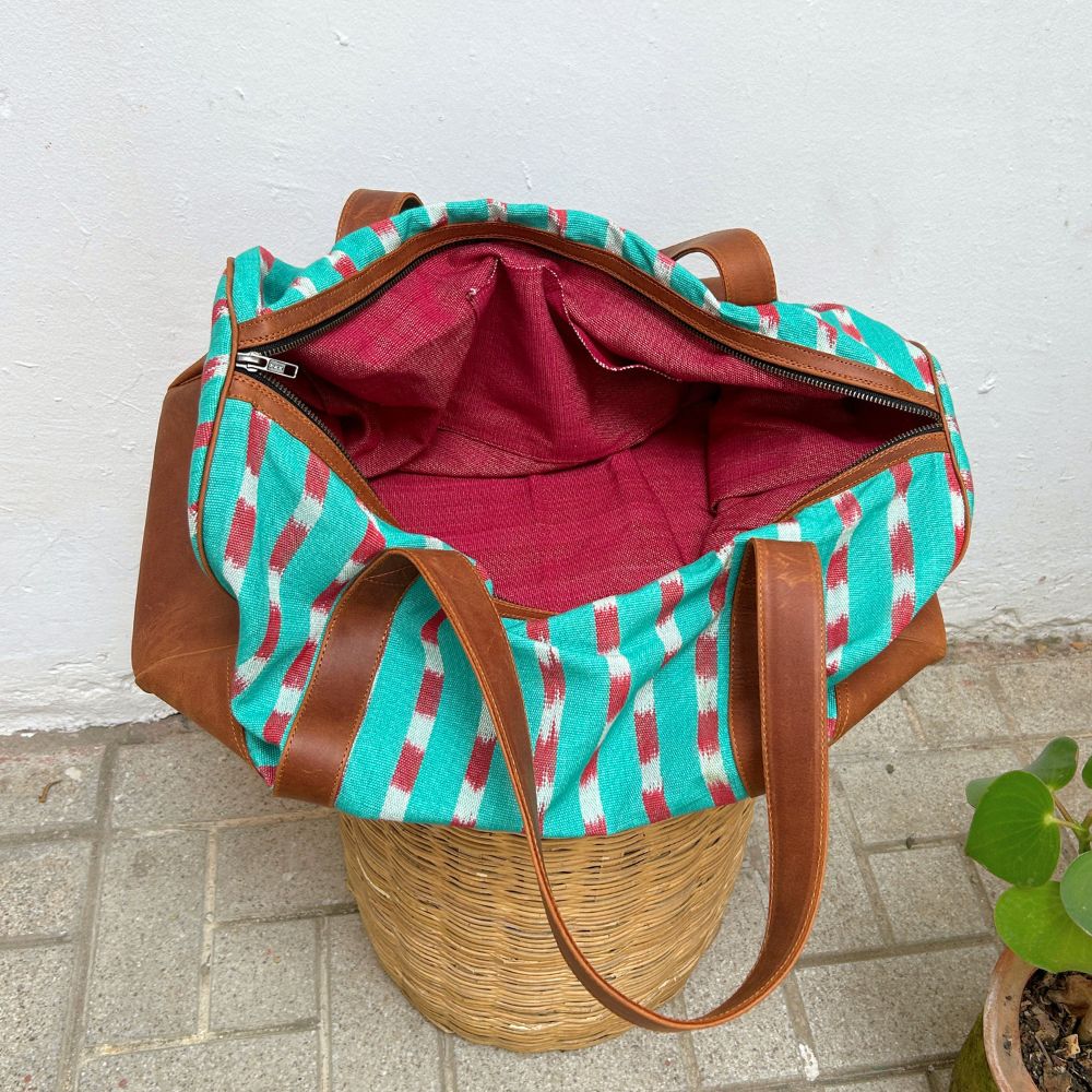 Duffel bag in green and red striped pattern with leather handles on a white background