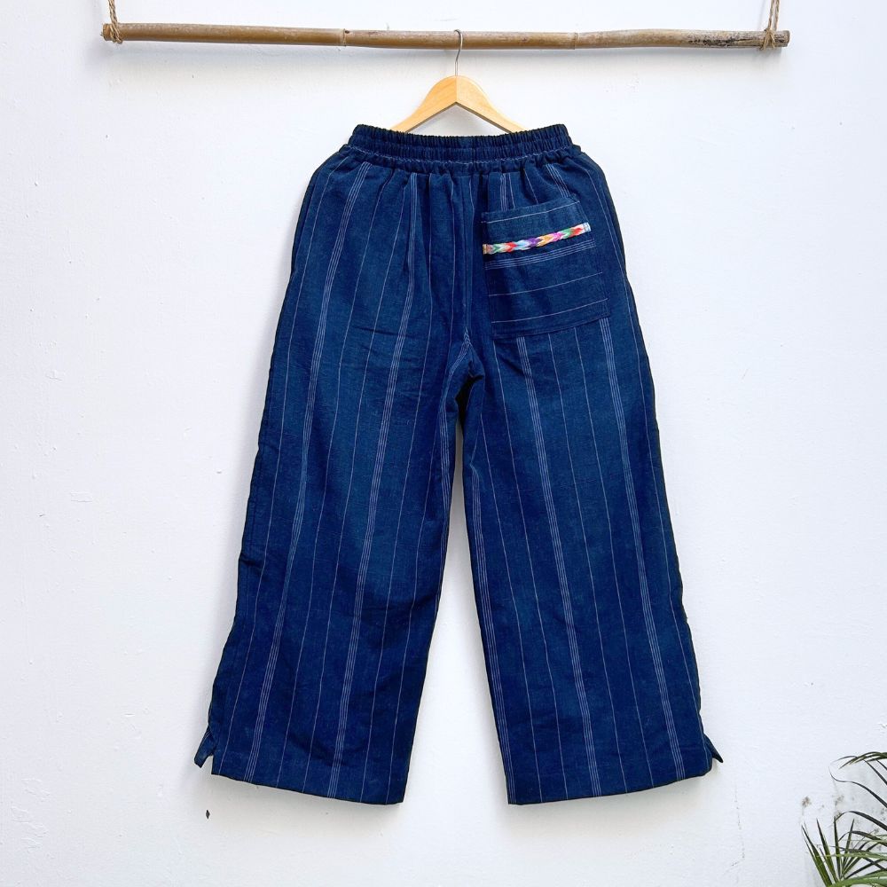 Navy pinstripe corte trousers with colorful randa on the sides, hanging on a wooden hanger against a white background.