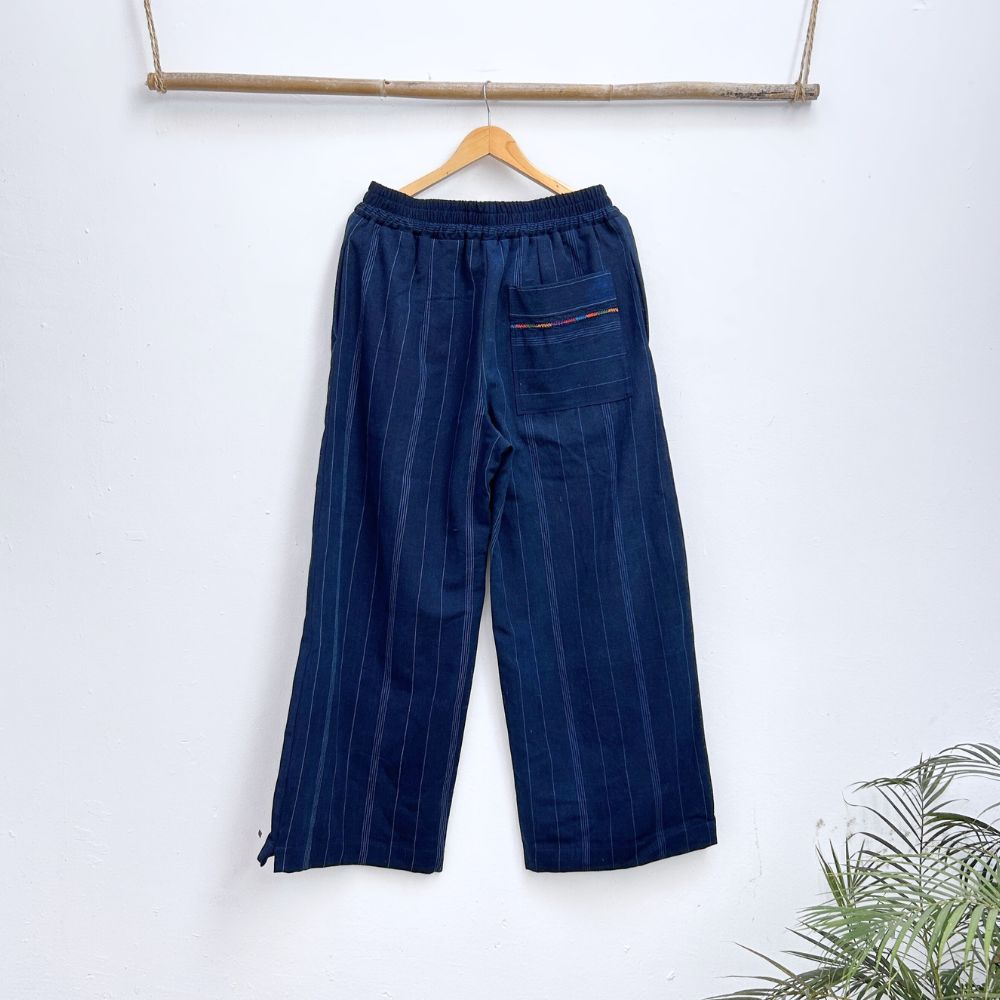 Navy pinstripe corte trousers with thin colorful randa on the sides, hanging on a wooden hanger against a white background.