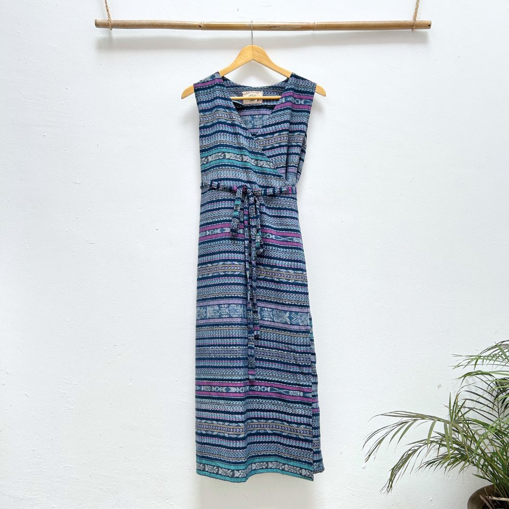 Blue patterned dress hanging on a wooden hanger against a white wall with a plant in the corner.
