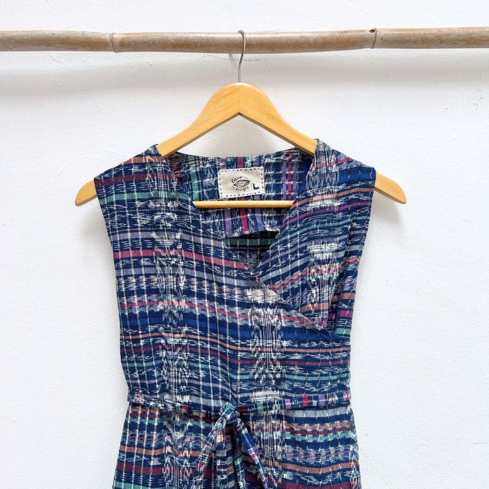 Blue patterned dress hanging on a wooden hanger against a white wall with a plant in the corner.
