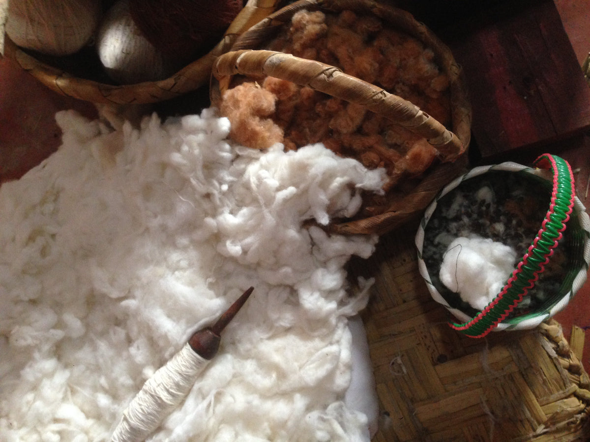 A cotton spindle, cotton fibers, and baskets on a wooden surface