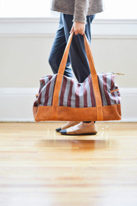Person holding a striped duffel bag with brown leather handles.