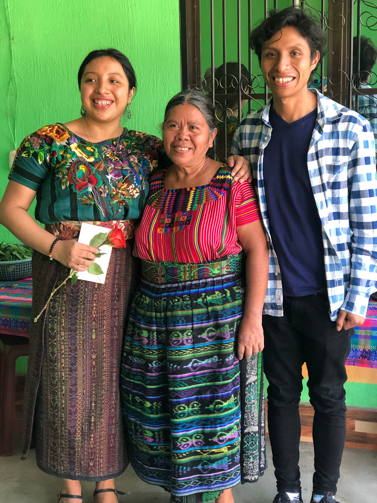 Three people in traditional clothing posing for a photo against a green wall.