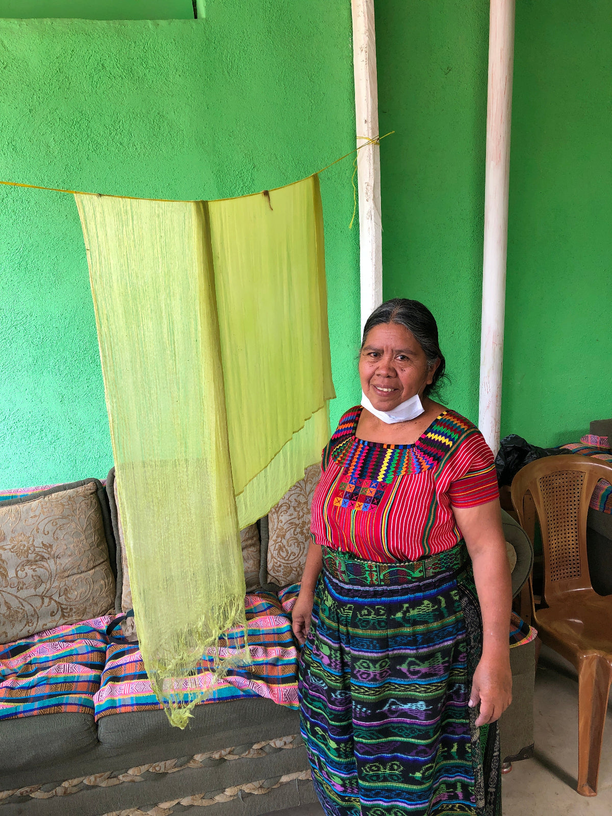 Woman in traditional clothing standing next to a green fabric in front of a green wall