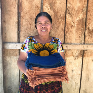 Woman holding folded handwovens against a wooden wall