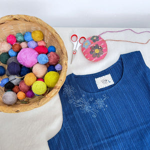 Colorful yarn balls in a basket, blue blouse, and sewing tools on a white surface