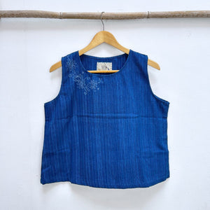 Blue sleeveless top with floral design on a wooden hanger against a white background