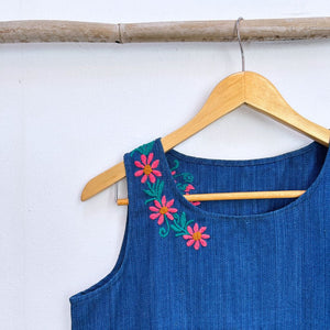 Blue sleeveless top with floral embroidery on a wooden hanger against a white background