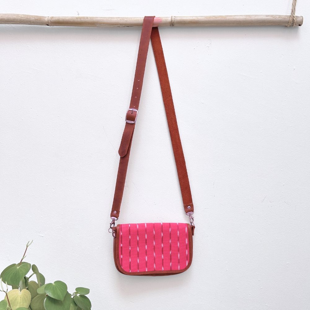 Pink woven handbag with brown strap on a white background