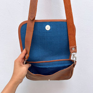 Brown leather crossbody bag with blue interior on a white background