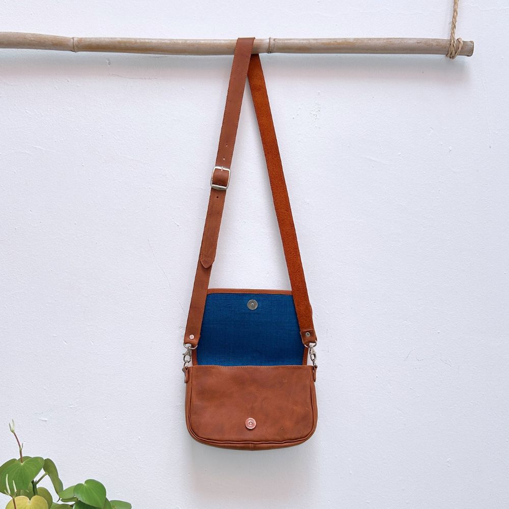 Brown leather crossbody bag with a blue interior on a white background