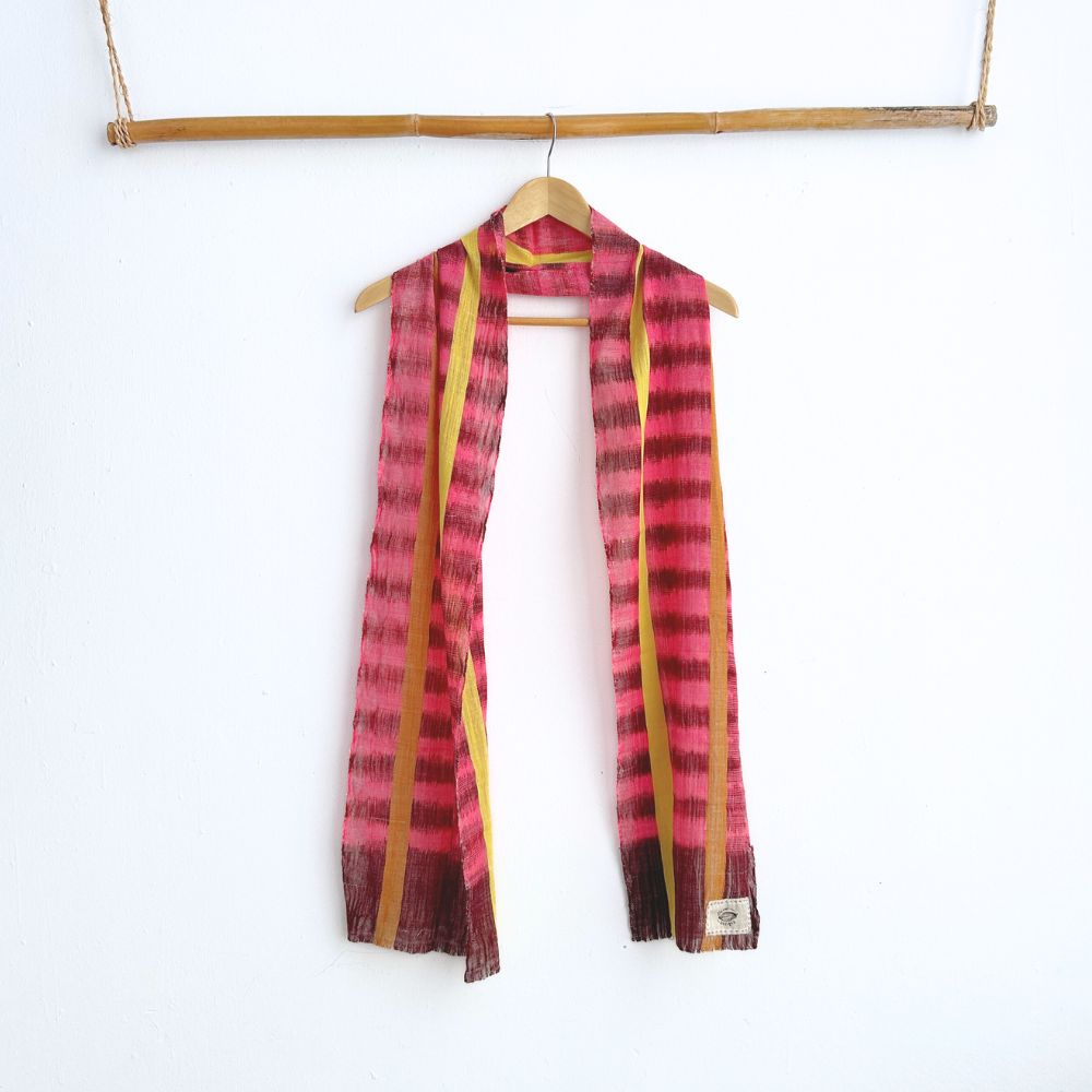 Pink and yellow ikat scarf hanging on a wooden hanger against a white background