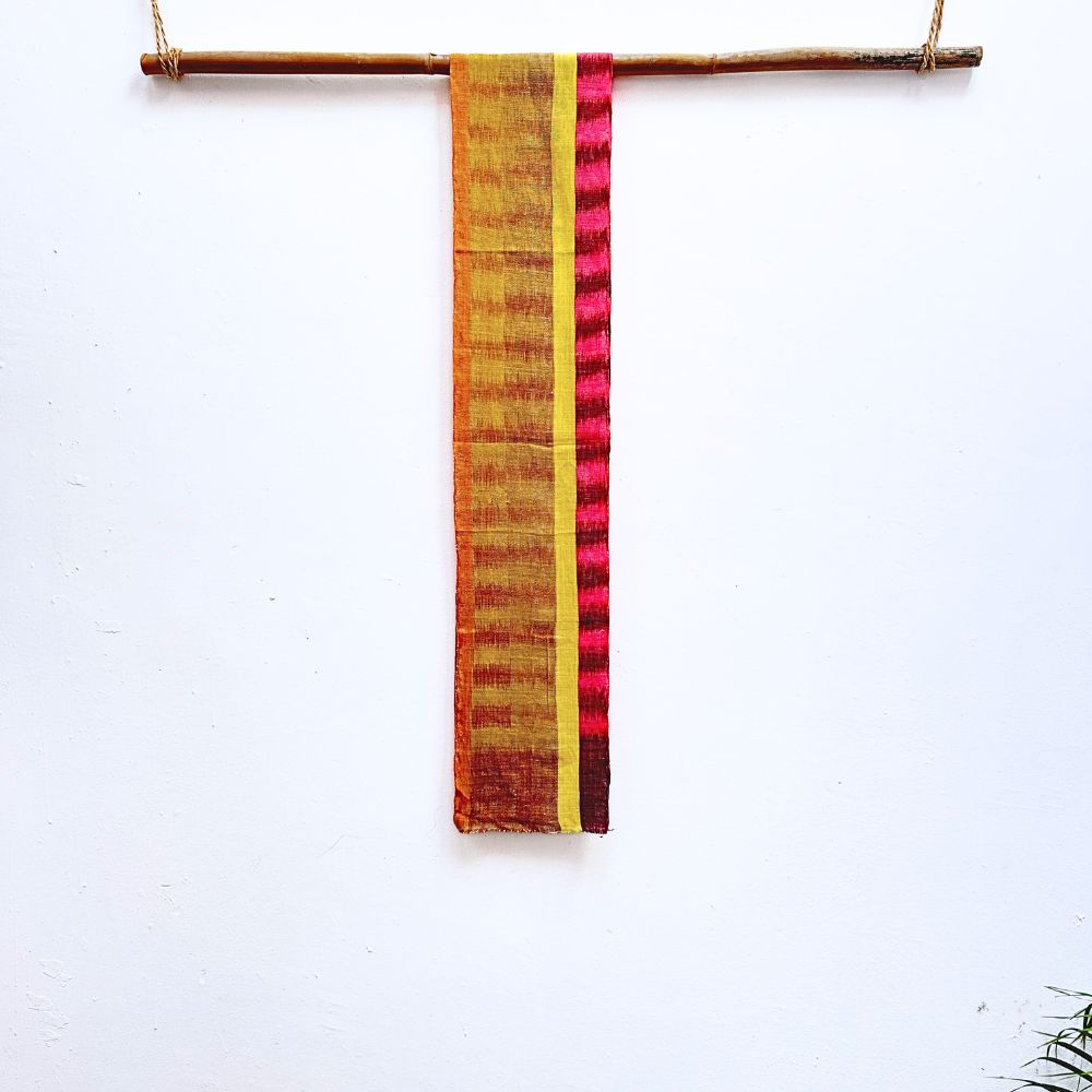Colorful fabric strip with yellow, red, and brown pattern hanging on a stick against a white background