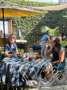 Two women enjoying the tamalitos they prepared during the class, seated at an outdoor table in the garden while sharing a meal together.