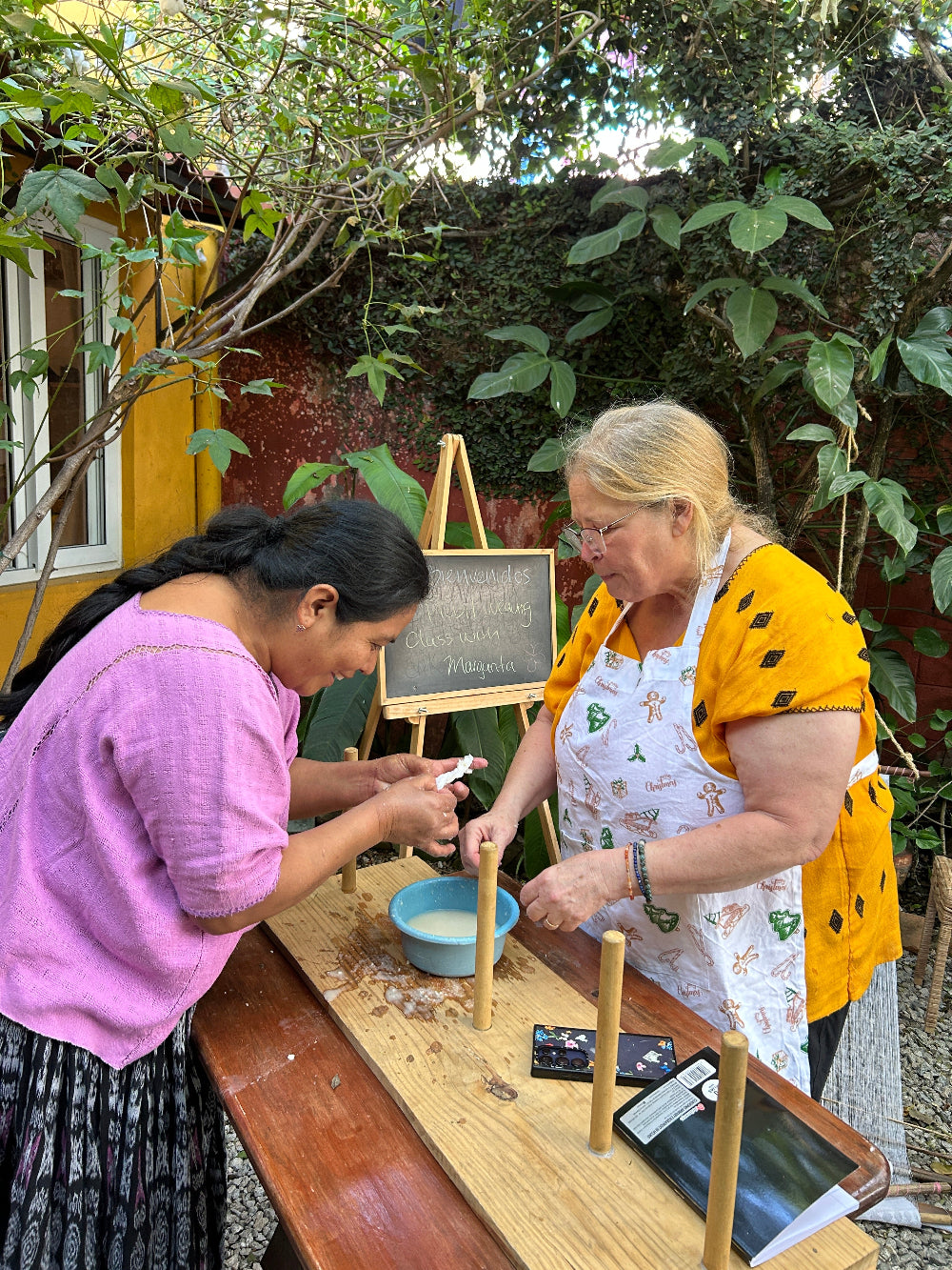 Two women starching thread together in the garden.