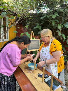 Two women starching thread together in the garden.