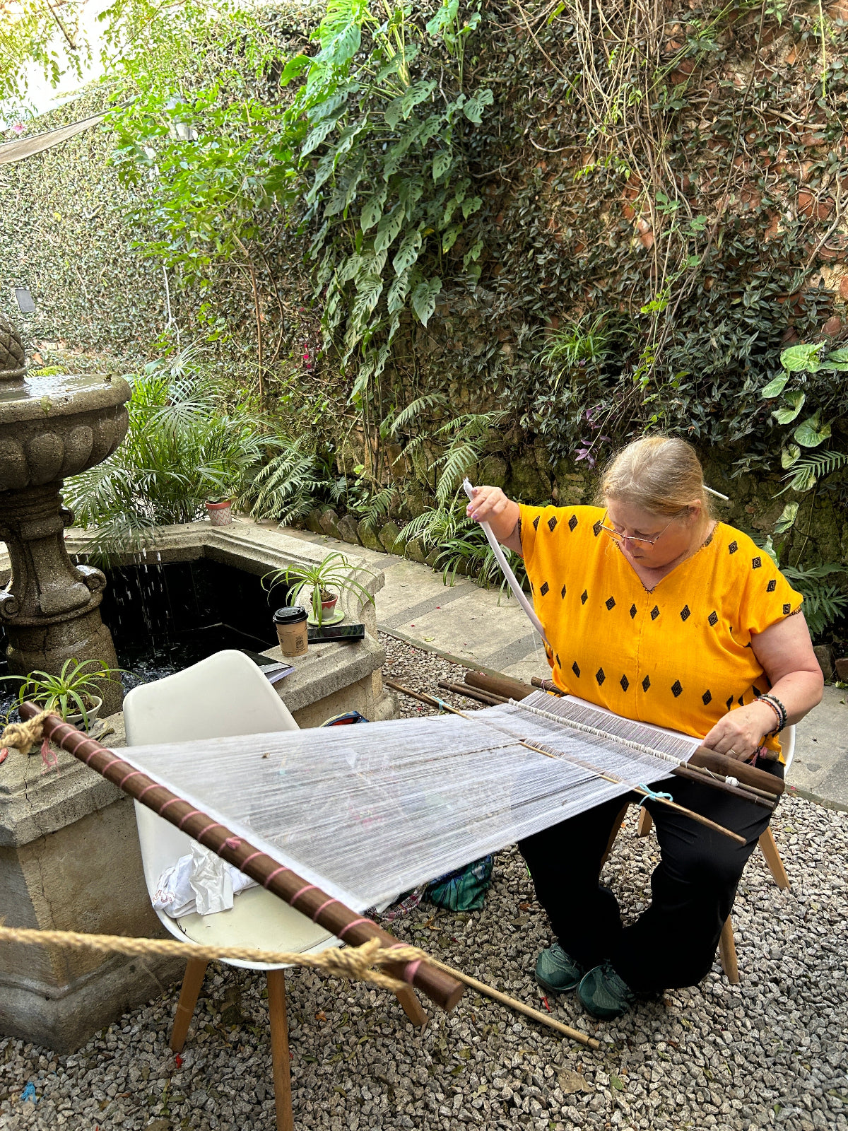 Student weaving on a large picbil loom in the garden.