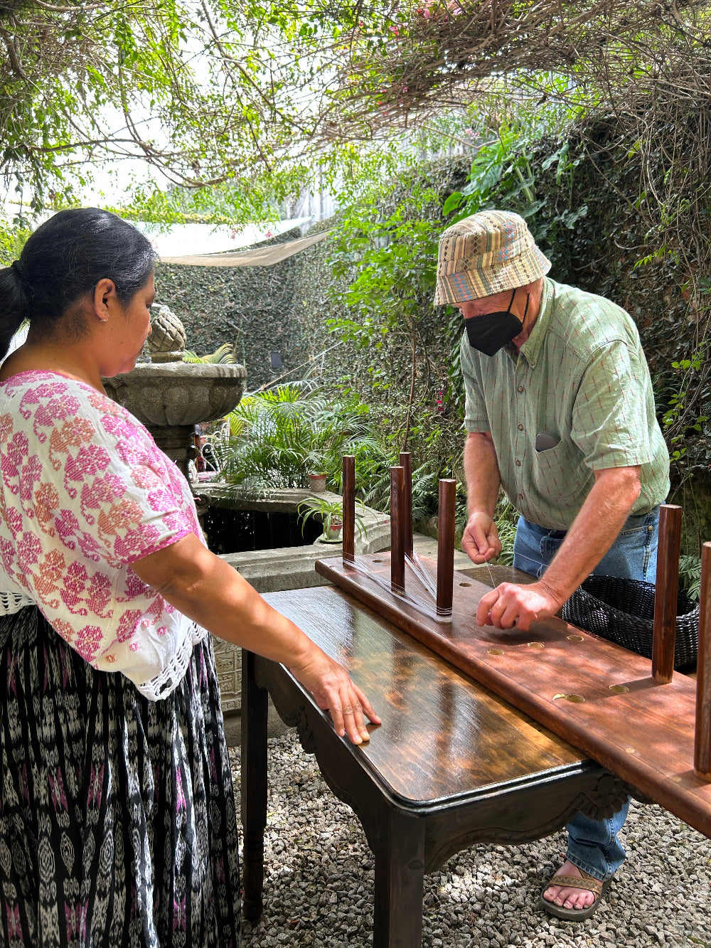 Two people standing near a wooden table outdoors with trees in the background