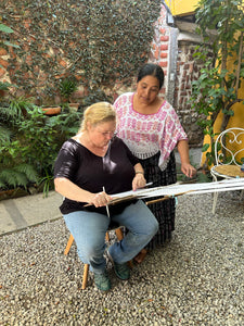 Two weavers in a lush garden weaving together.