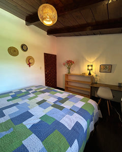 Bed with a geometric patterned quilt in a room with wooden walls and a lamp.