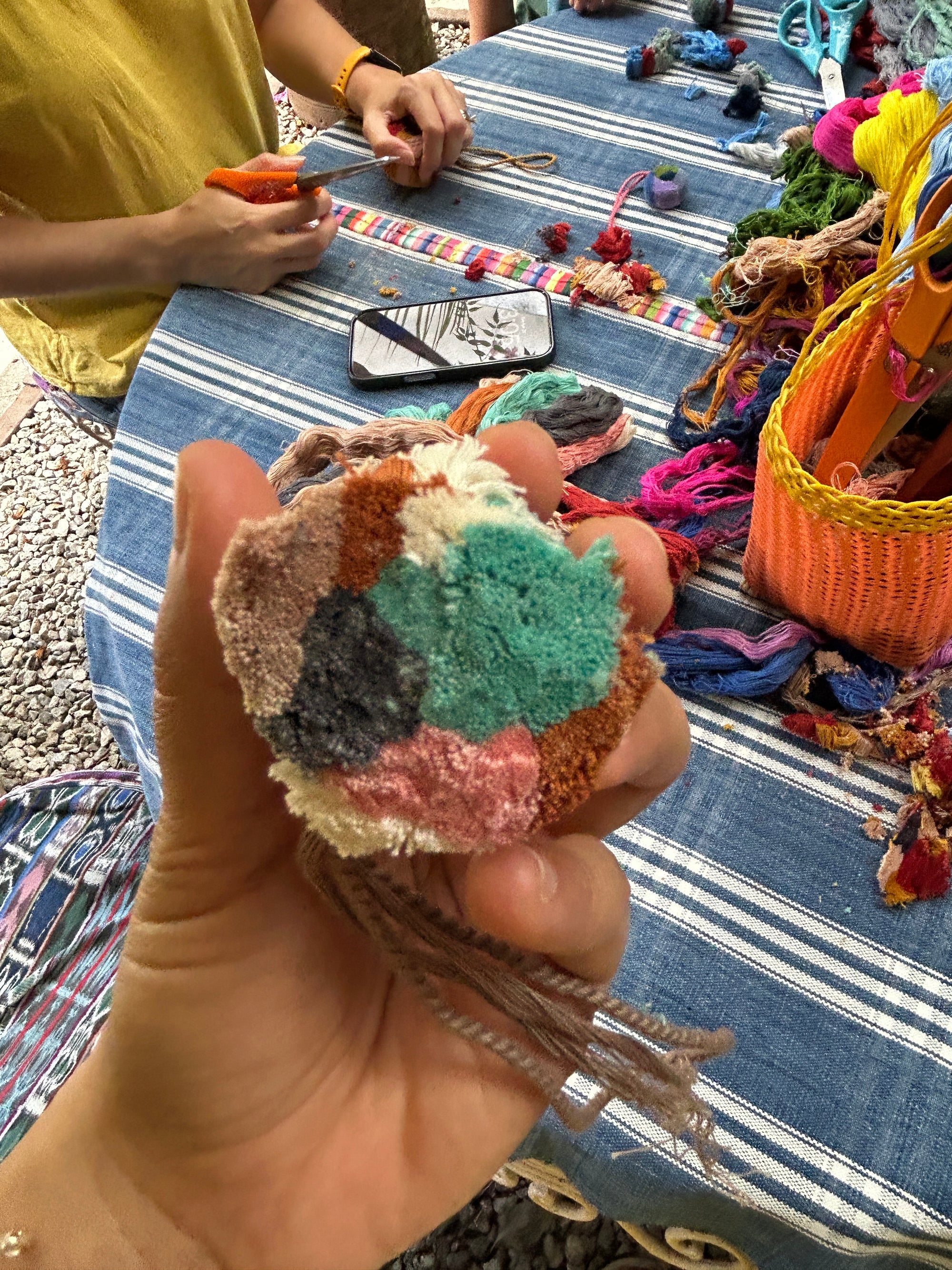 Close-up of the early stages of pompom making, showing freshly cut and gathered yarns being prepared for assembly. The yarn colors are mostly neutral, with touches of pink and turquoise.