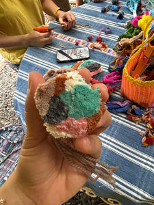 Close-up of the early stages of pompom making, showing freshly cut and gathered yarns being prepared for assembly. The yarn colors are mostly neutral, with touches of pink and turquoise.
