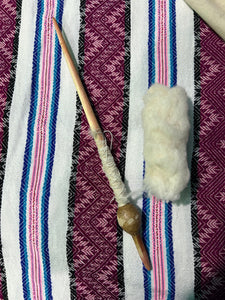 A traditional wooden spinning tool with a wooden bobbin and a bundle of white cotton fiber, laid out on a colorful woven textile background.