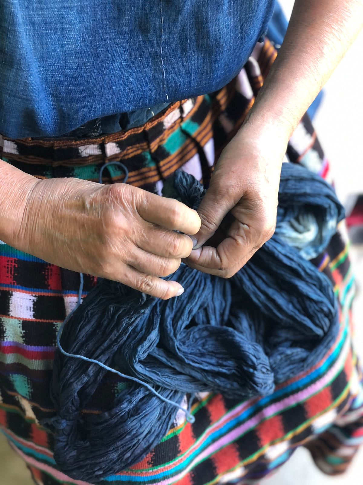Person holding a skein of indigo-dyed yarn with a colorful patterned apron.