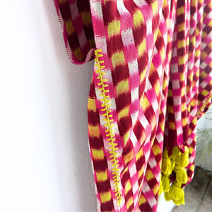Colorful checkered handwoven ikat cotton textile draped on a white wall, showing embroidery in yellow