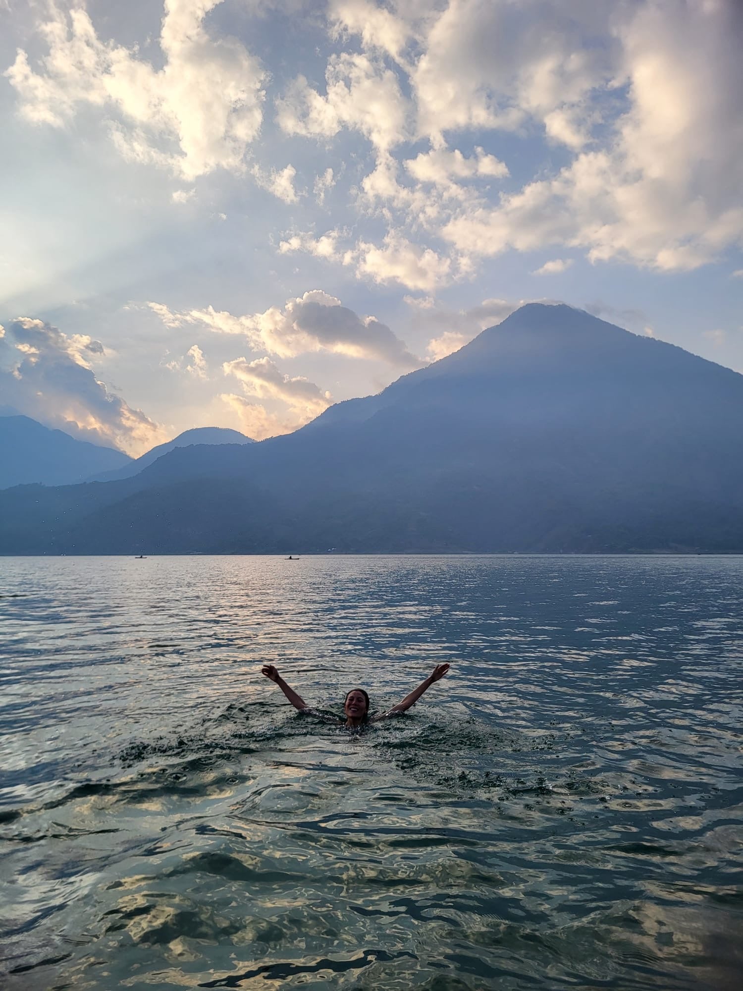 A person swimming in a lake with mountains in the background.