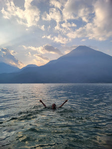 A person swimming in a lake with mountains in the background.